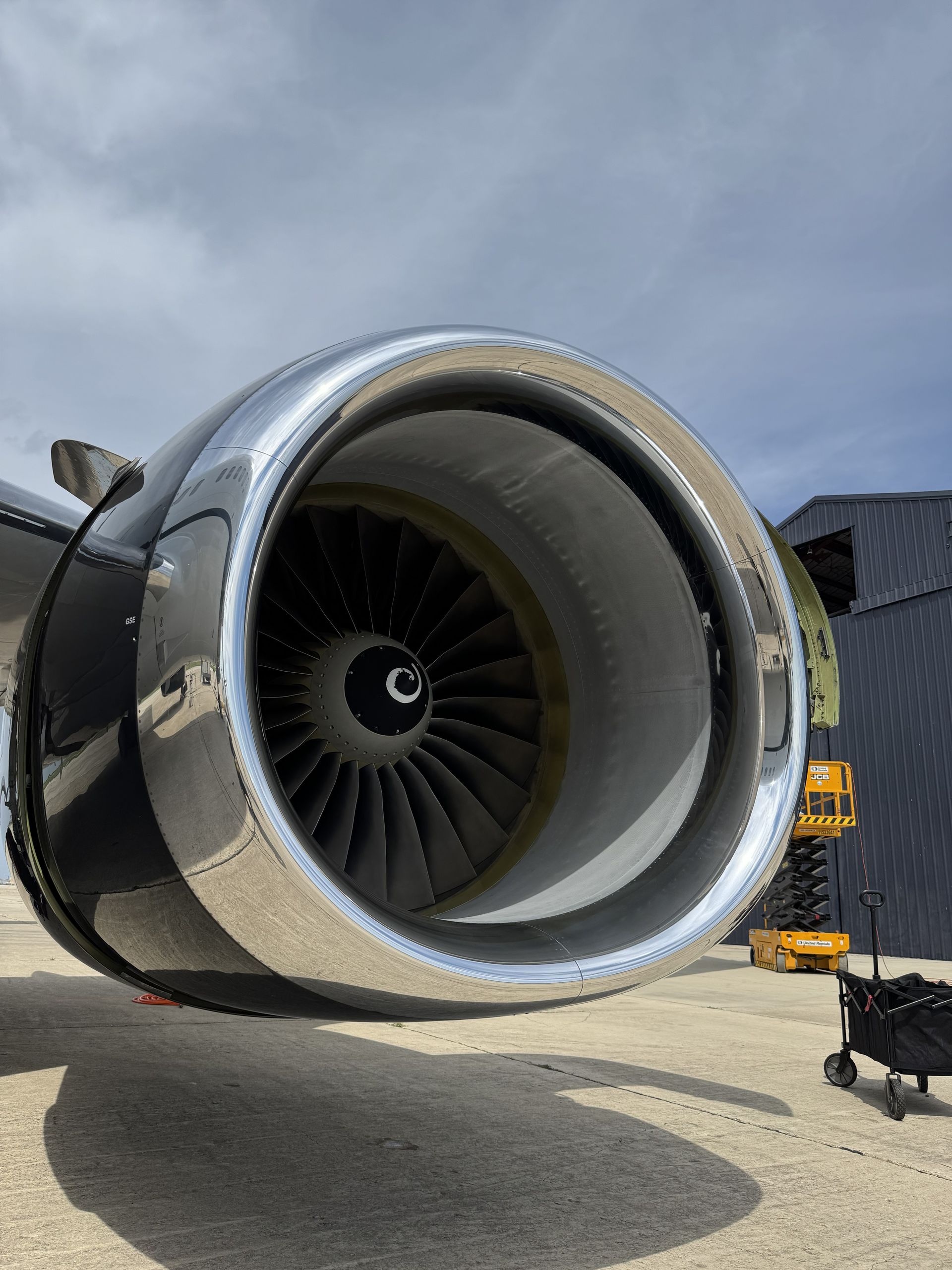 Close-up of a jet engine on an airplane wing at an airport, with a cloudy sky.