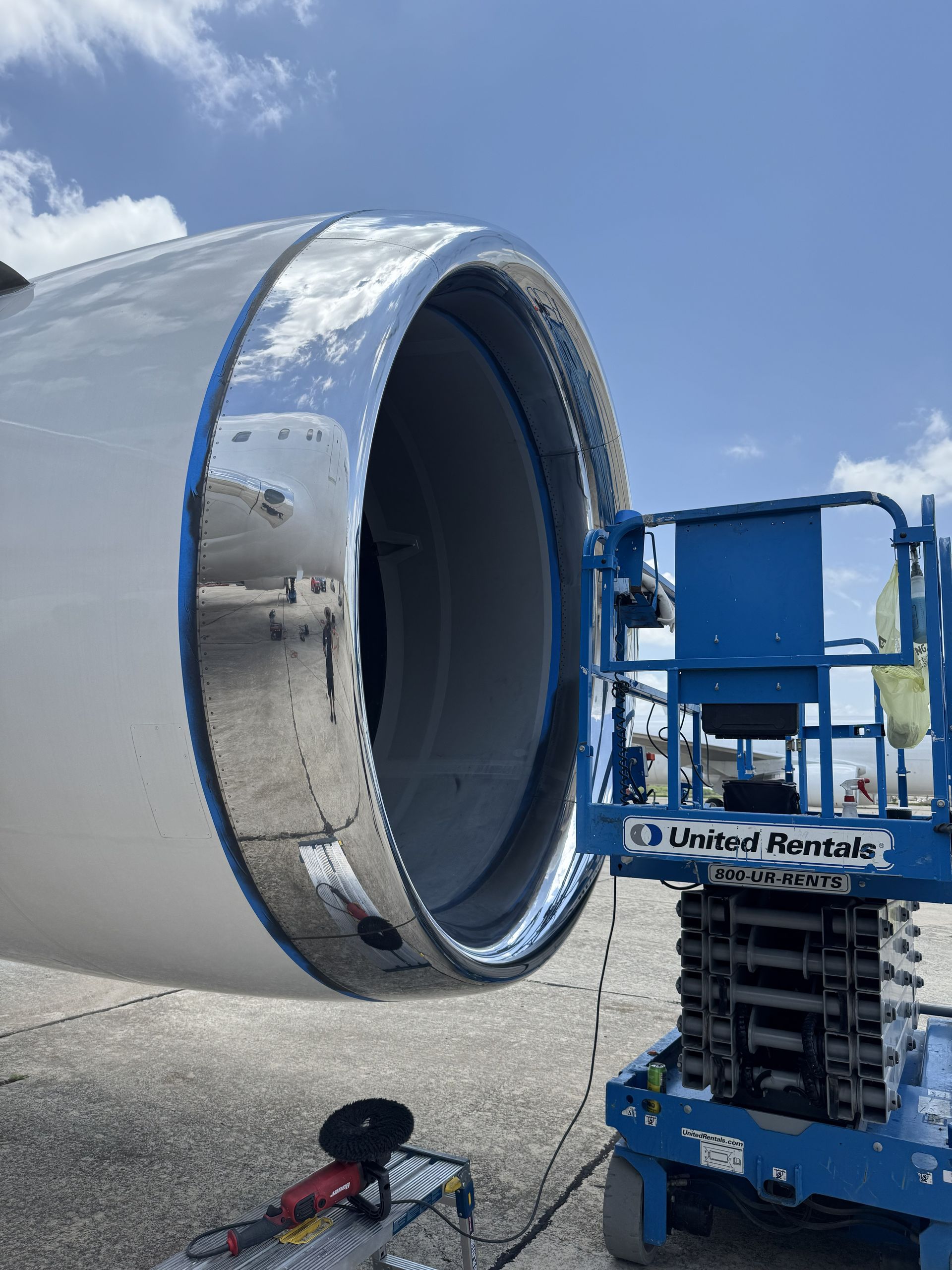 Airplane engine nacelle being serviced on a blue lift in a sunny tarmac area