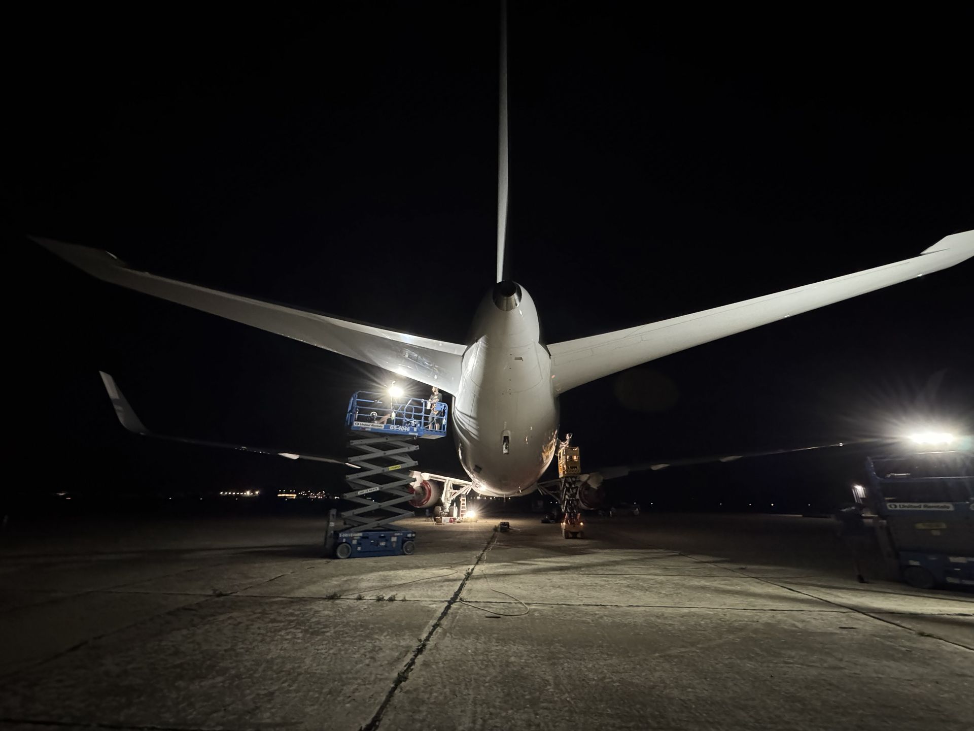 Airplane parked at night on a dimly lit tarmac, viewed from behind with wings spread wide.