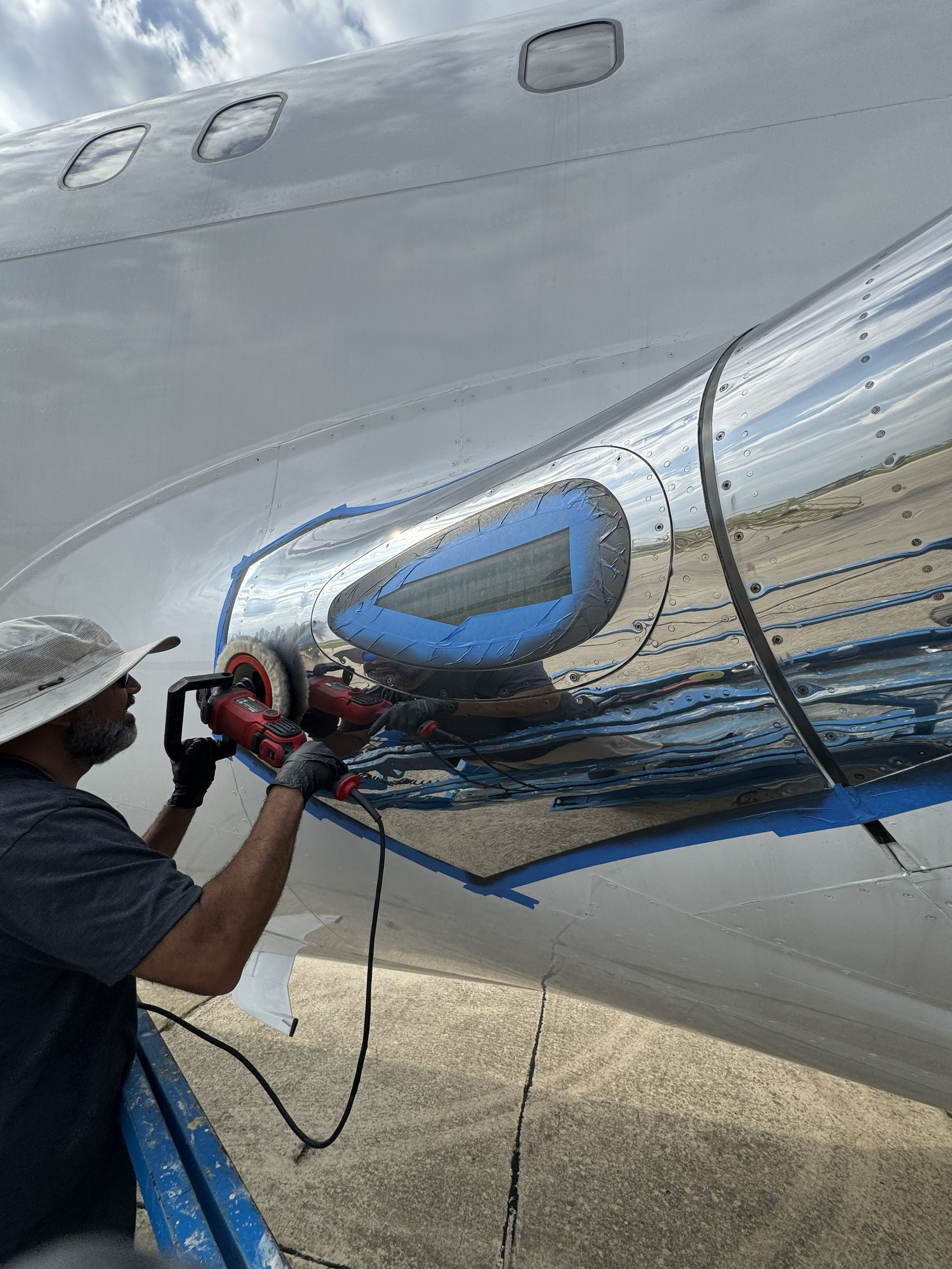 Worker polishing a silver airplane fuselage with a machine near a blue window panel
