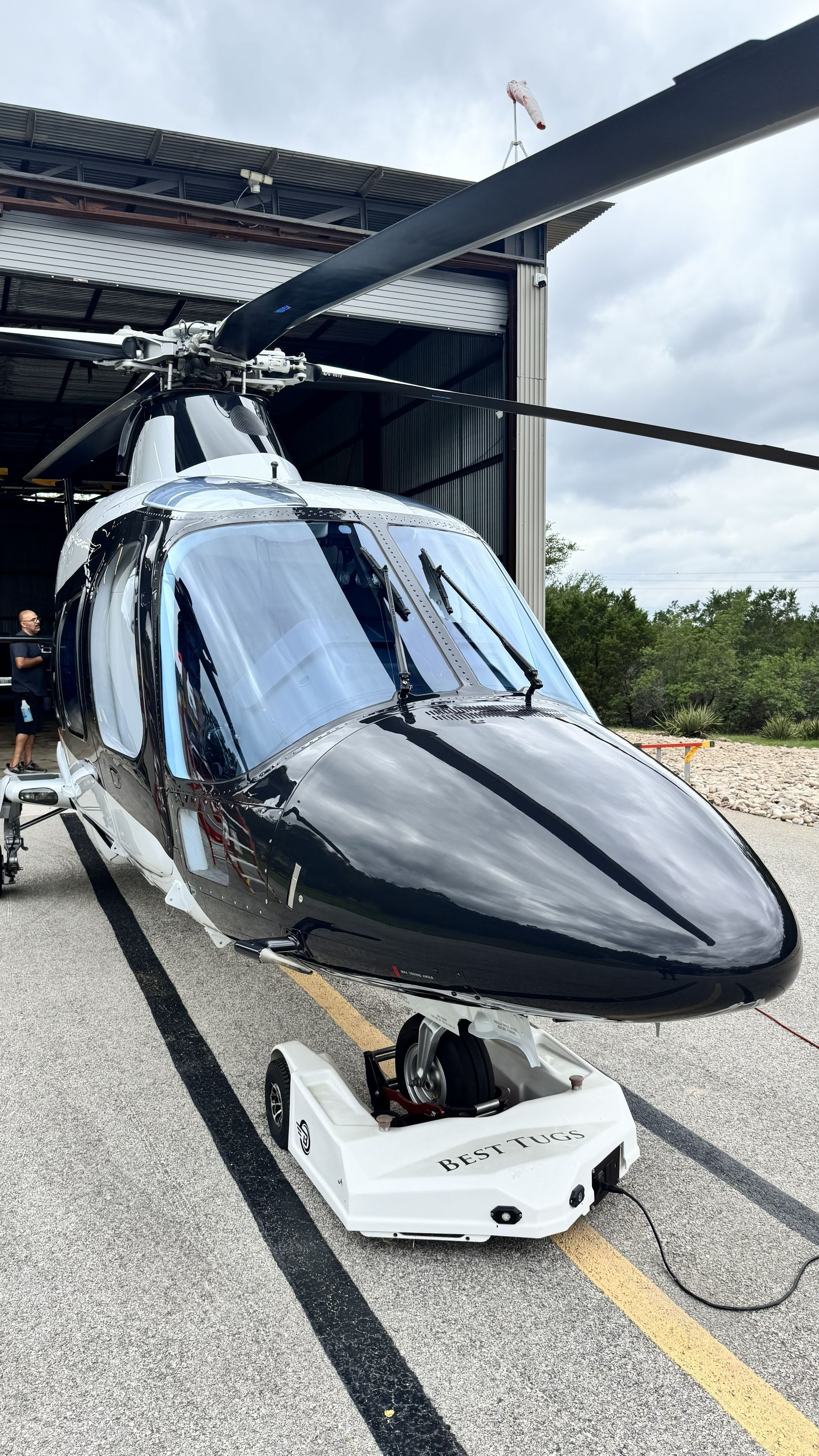 Black helicopter parked on tarmac under a hangar roof, front view with reflections.