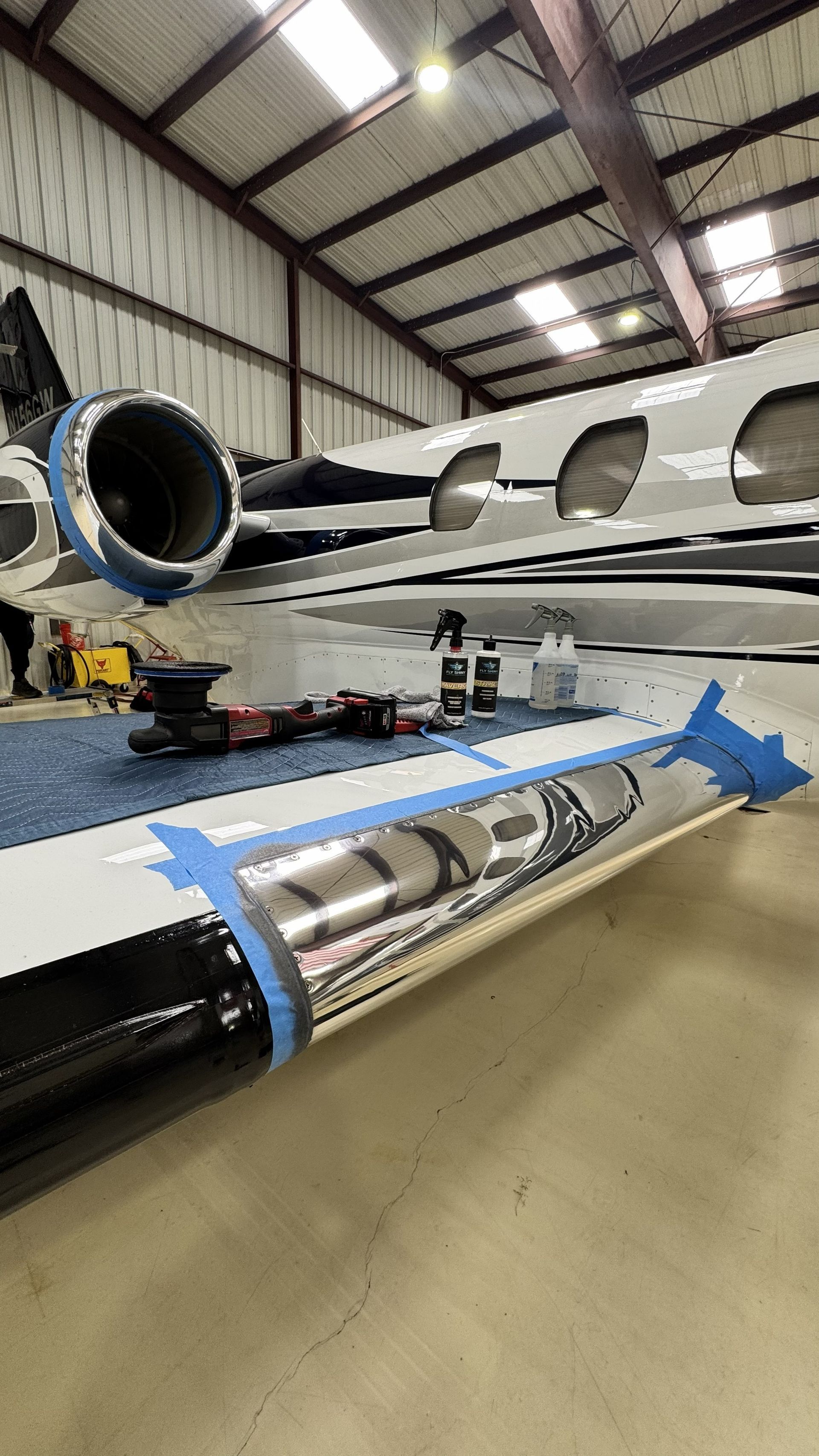 Interior of a hangar with a small jet and a blue-wrapped wing section in the foreground