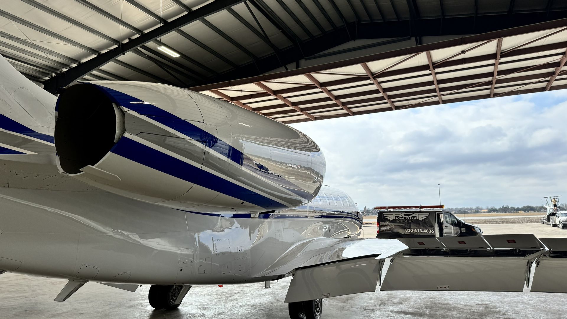Private jet under a hangar roof with blue stripes and an attached stairway on the tarmac