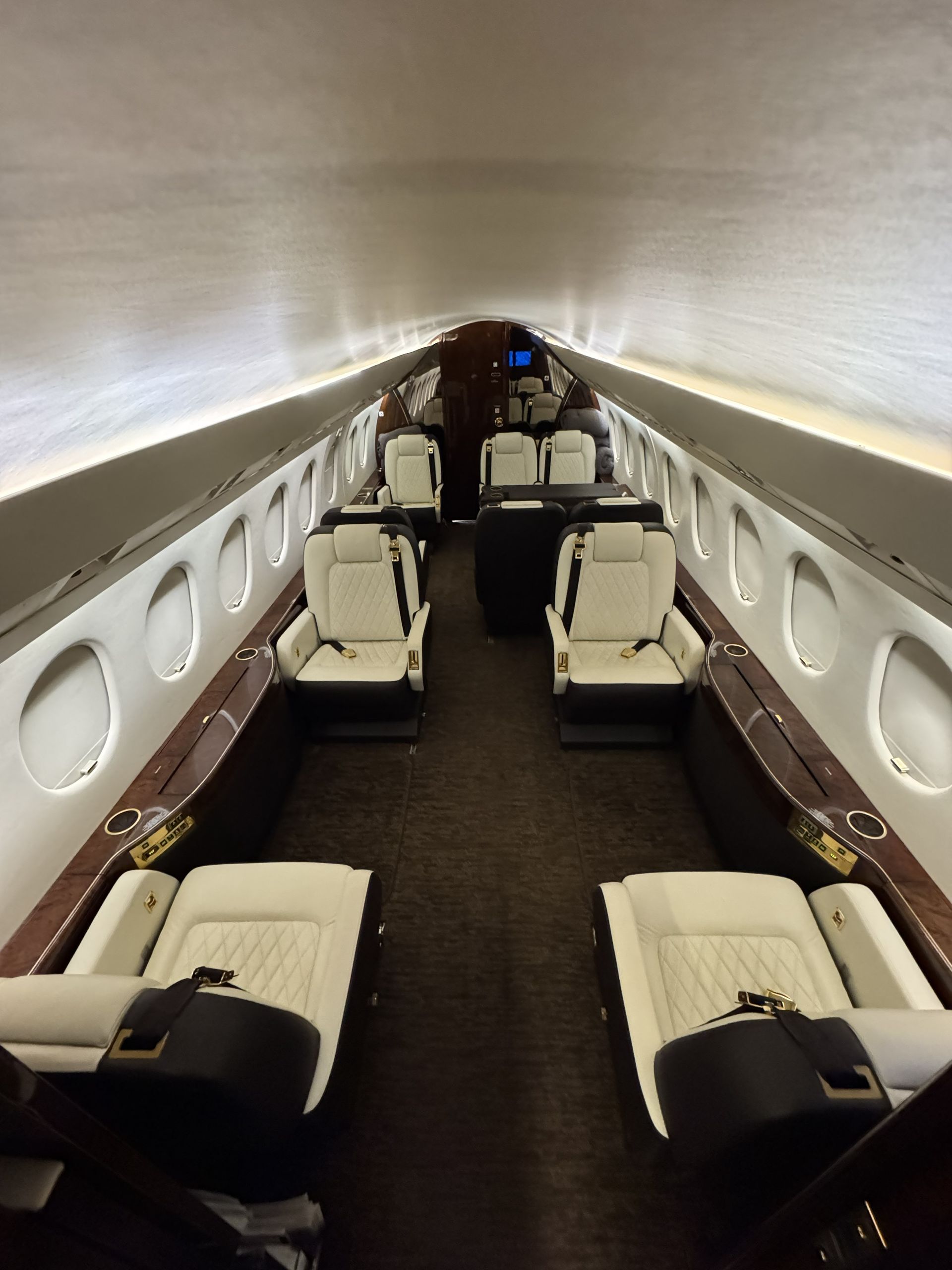 Luxury jet cabin with rows of cream seats and a curved beige ceiling in a narrow aisle.