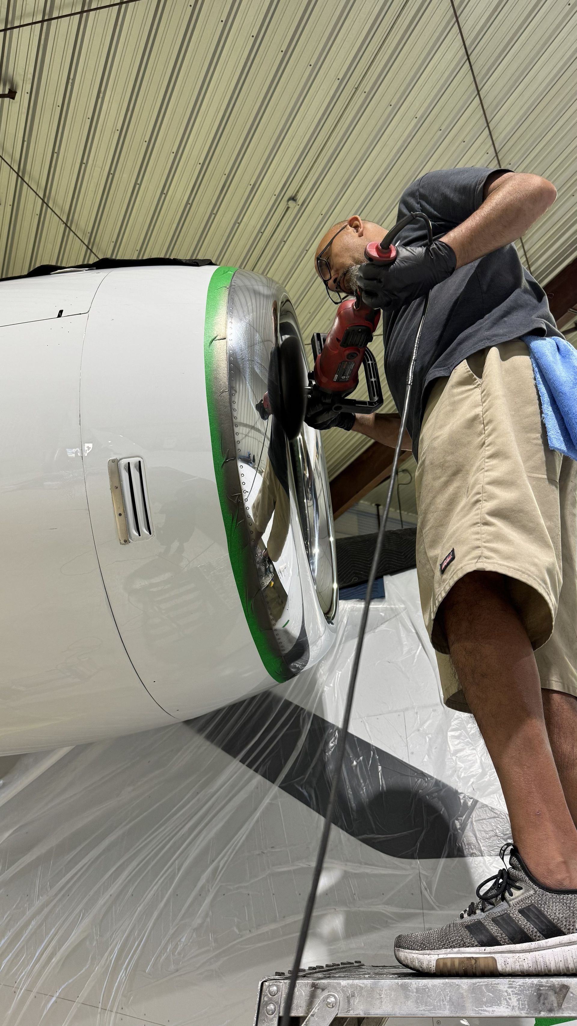 Person using a power tool to work on a large white cylindrical object indoors.