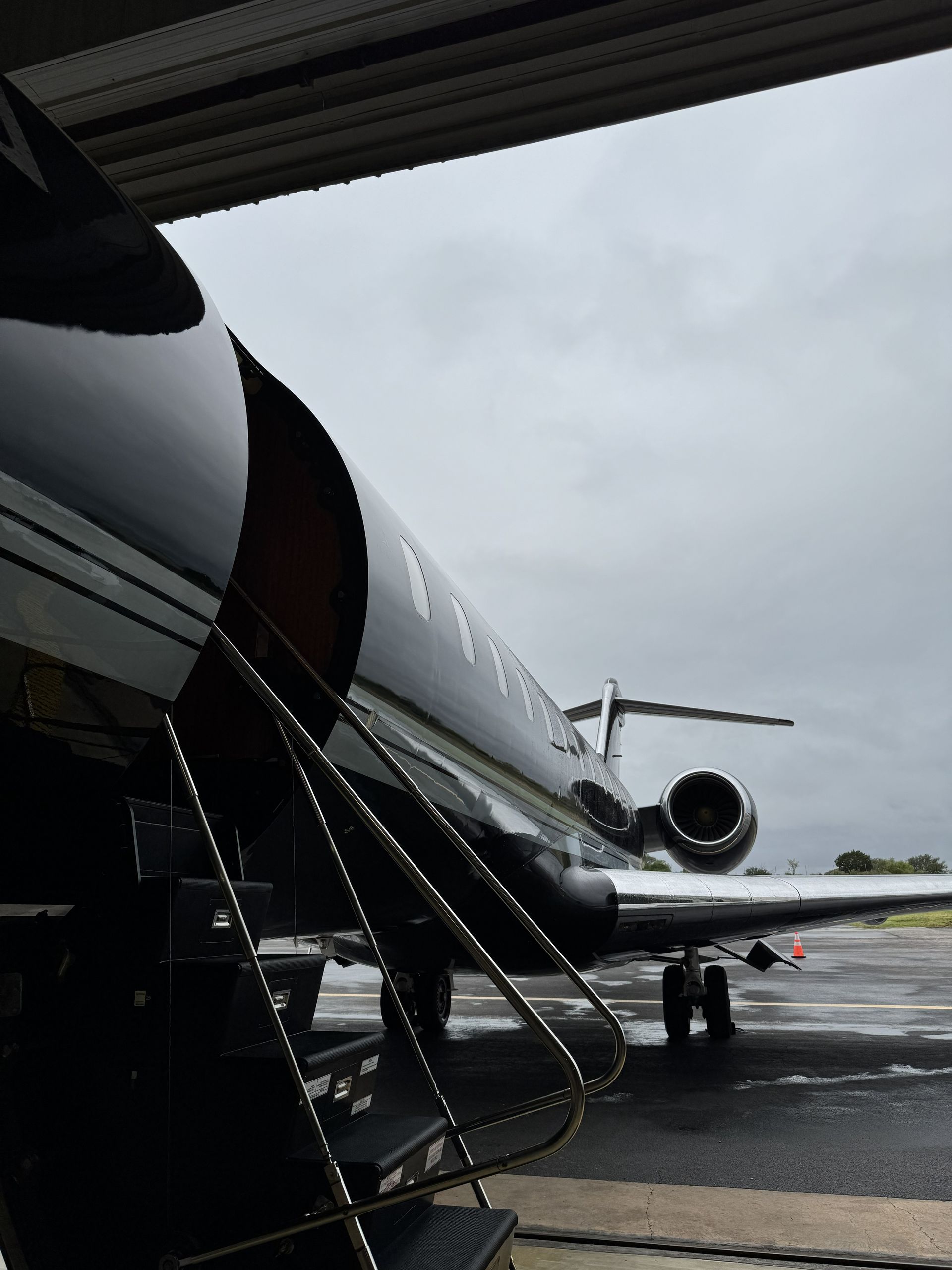Private jet on wet tarmac under an overcast sky, seen from an aircraft doorway