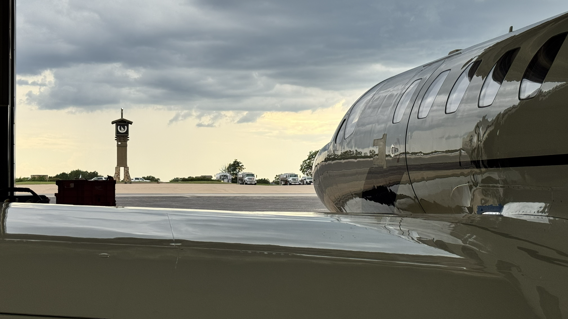 Airplane wing and engine beside a runway, with a distant tower under a cloudy sky