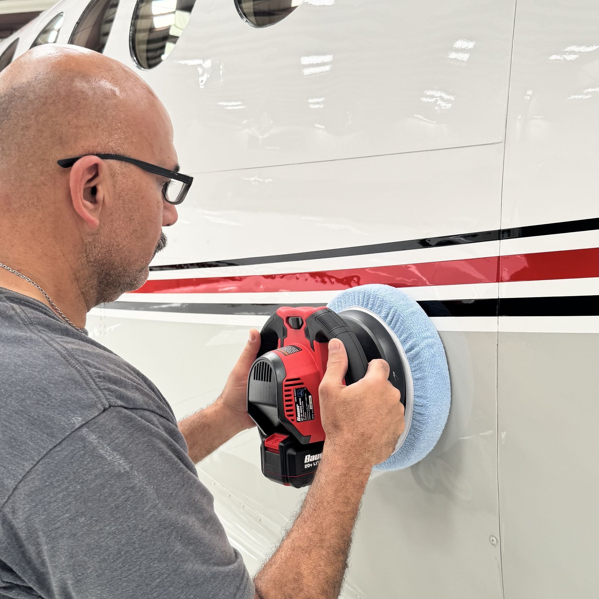Person polishing a white vehicle with a red power buffer and blue pad