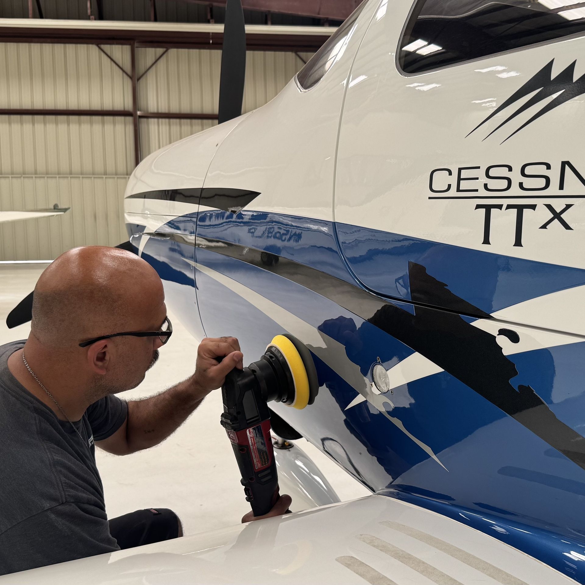 Man polishing the side of a white Cessna aircraft with blue stripes in a hangar