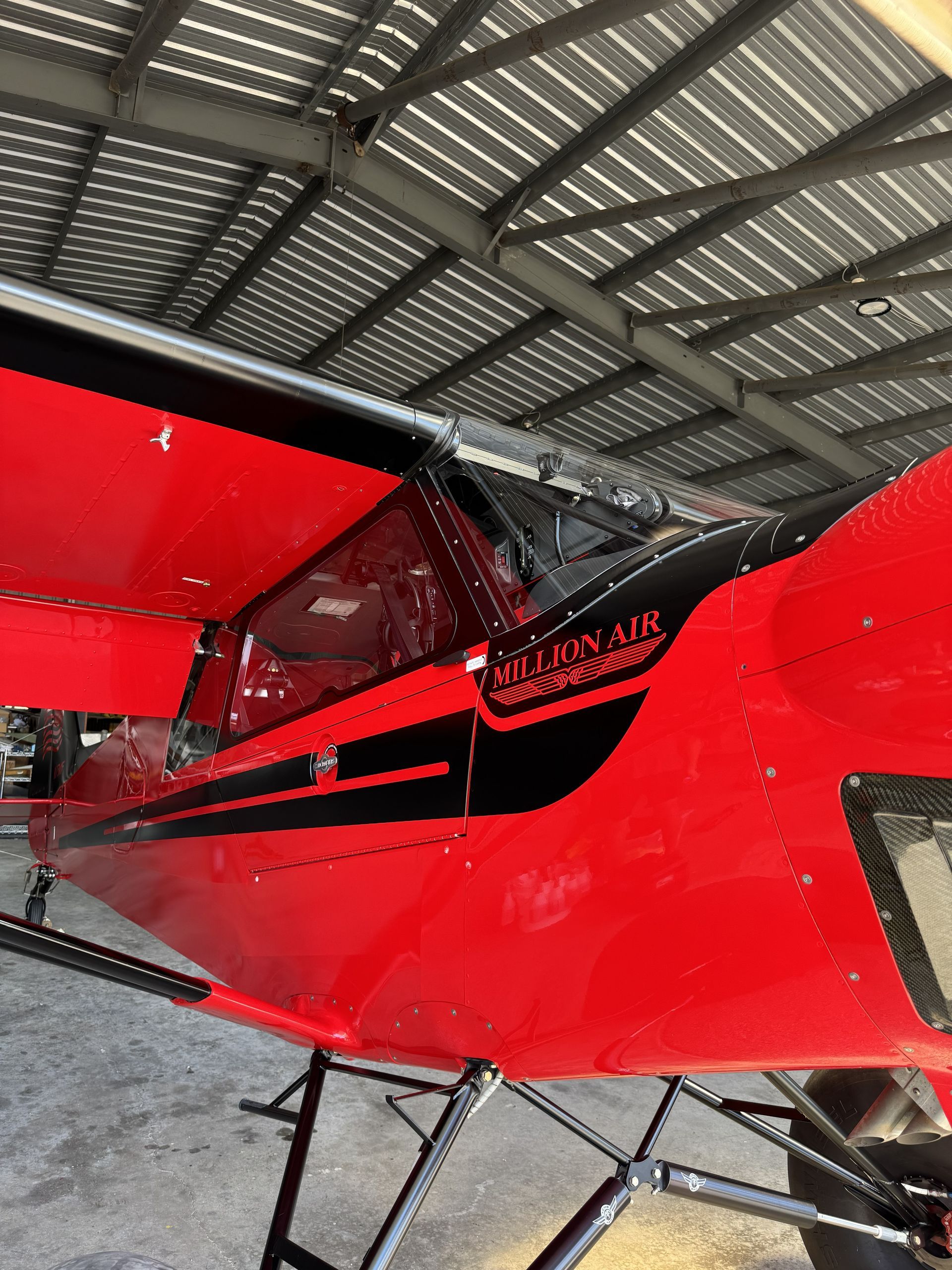 Red small airplane inside a hangar, with a red wing and black canopy visible.