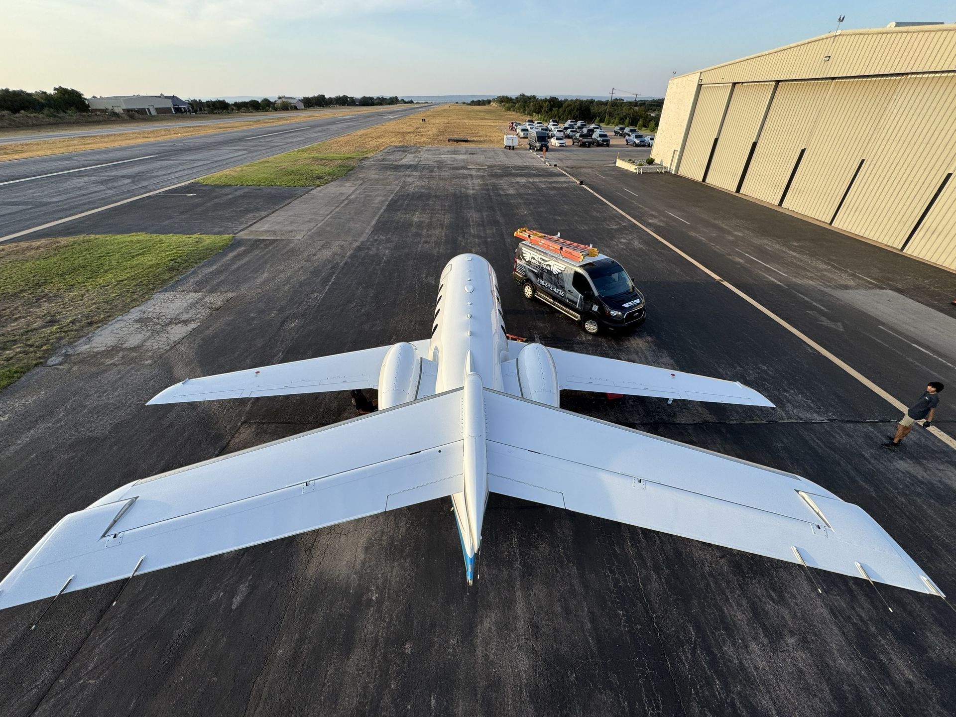 White jet parked on an airport tarmac beside a hangar, with a service vehicle nearby.