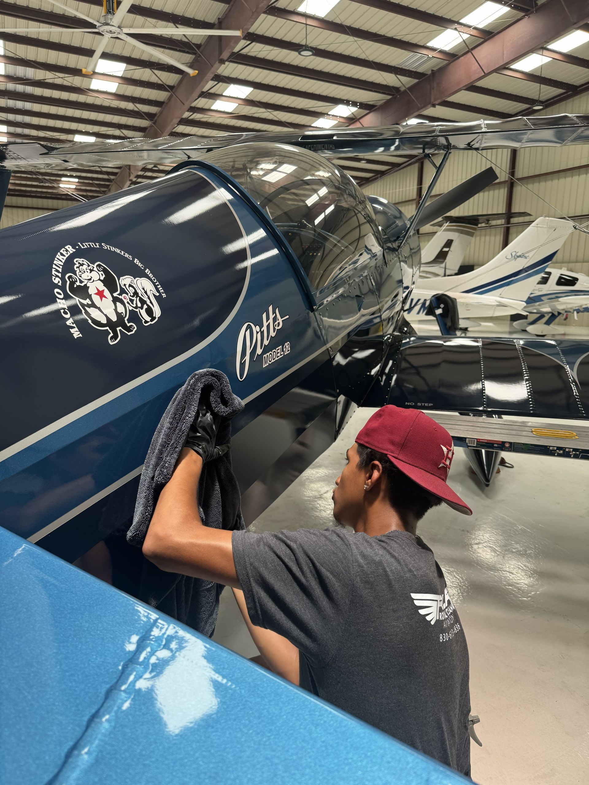 Person polishing a blue airplane in a hangar, with another aircraft in the background