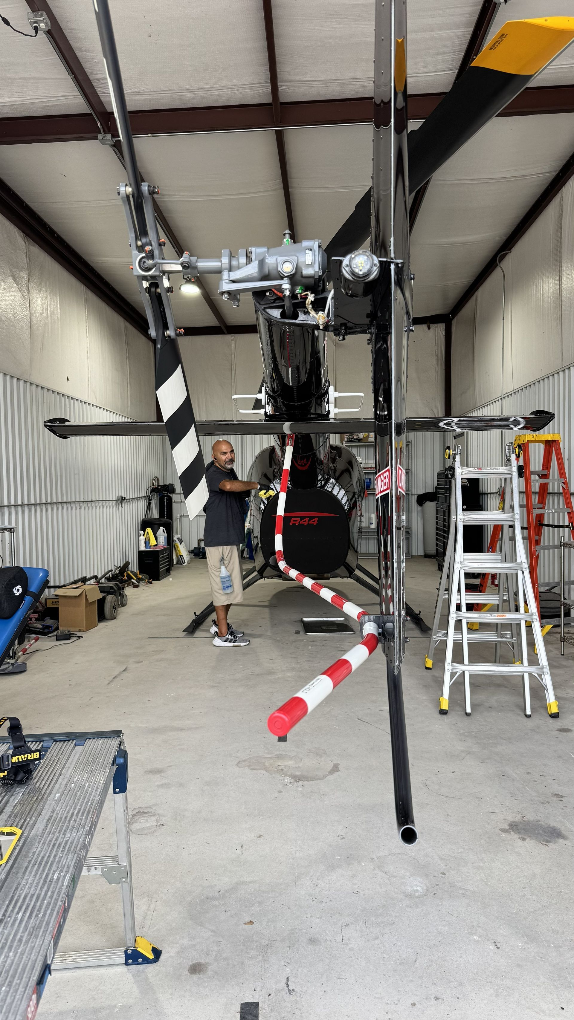 Inside a workshop, a partially assembled drone or machinery frame hangs above tools and ladders.