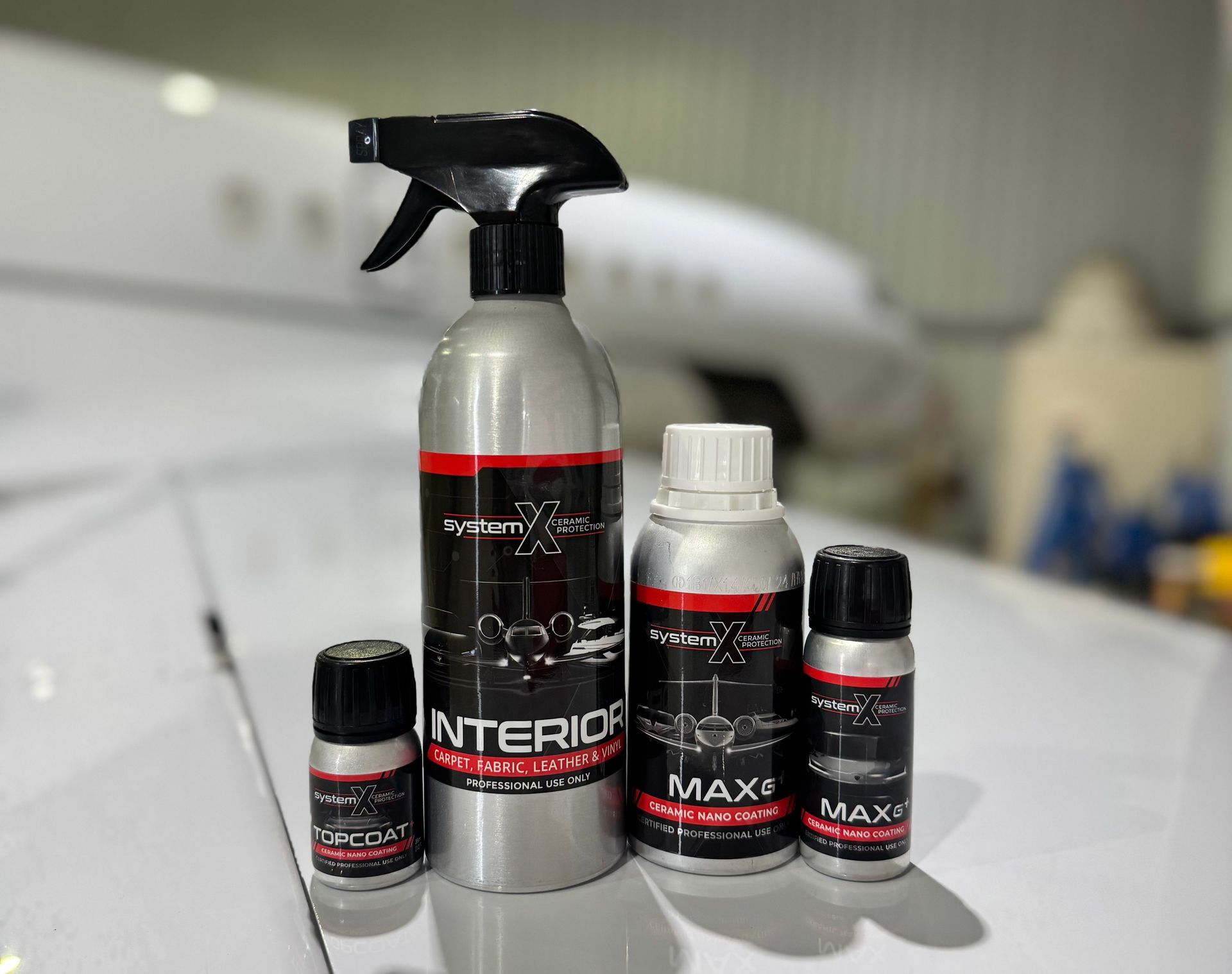 Car care spray bottles on a car hood, including a tall black trigger bottle and two small black-labeled bottles.