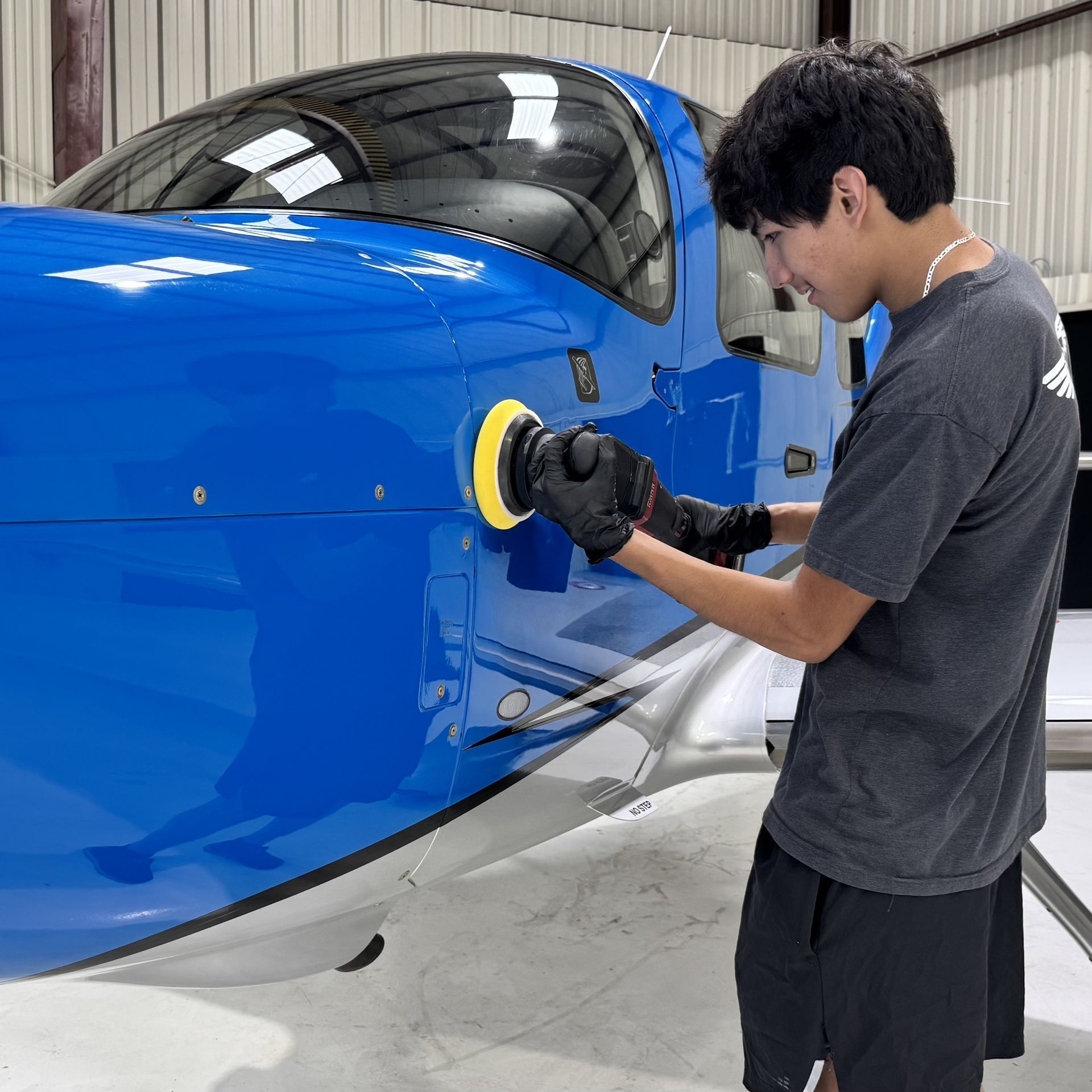 Person polishing a blue airplane nose in a hangar with a handheld buffer