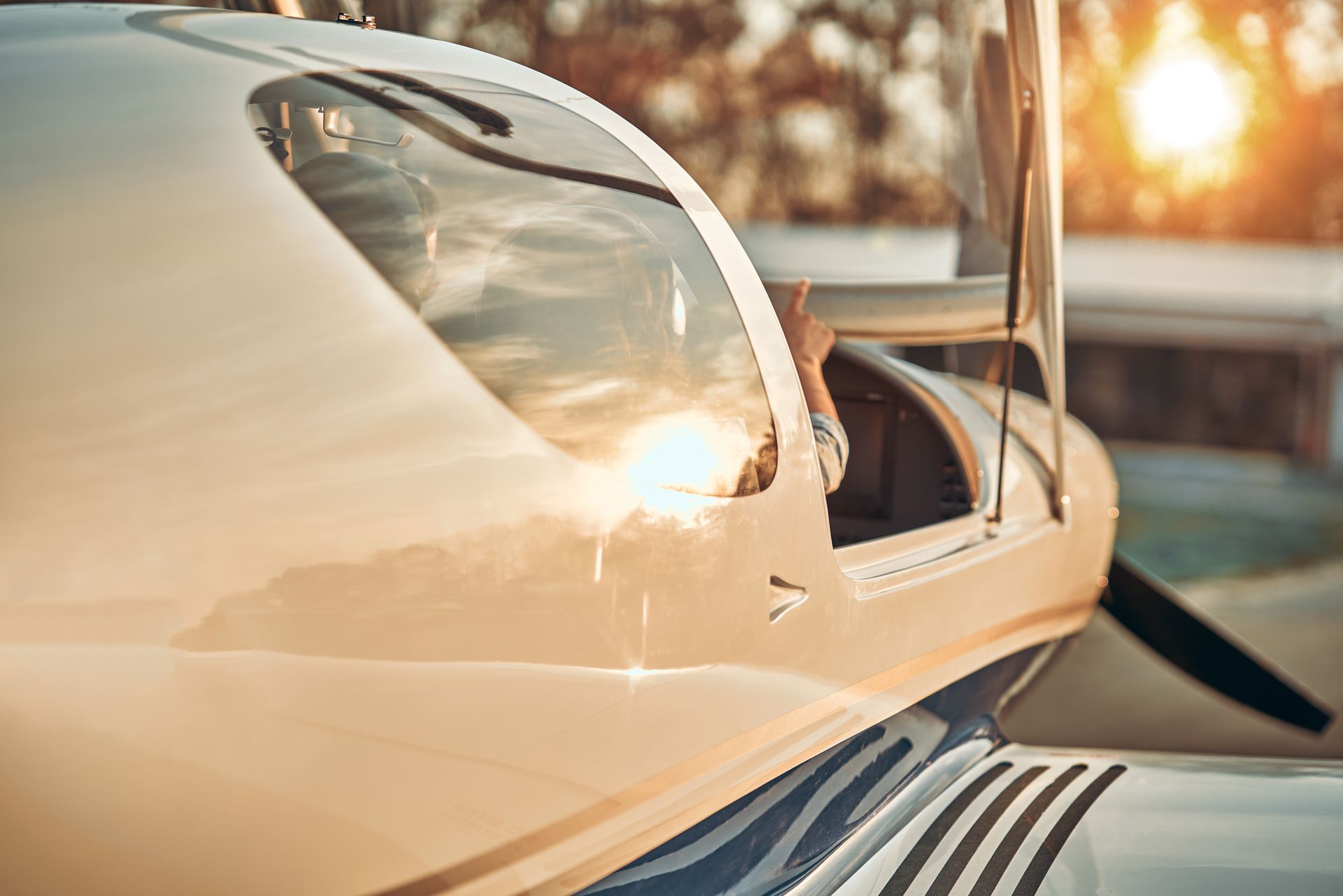 Close-up of a cream-colored airplane cockpit at sunset, with the canopy open and runway in the background