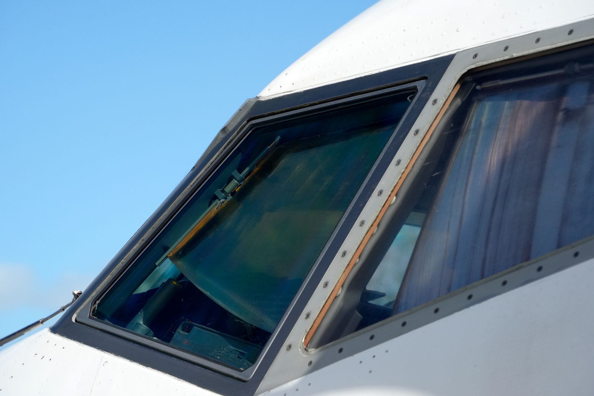 Airplane cockpit windows on a white fuselage against a blue sky