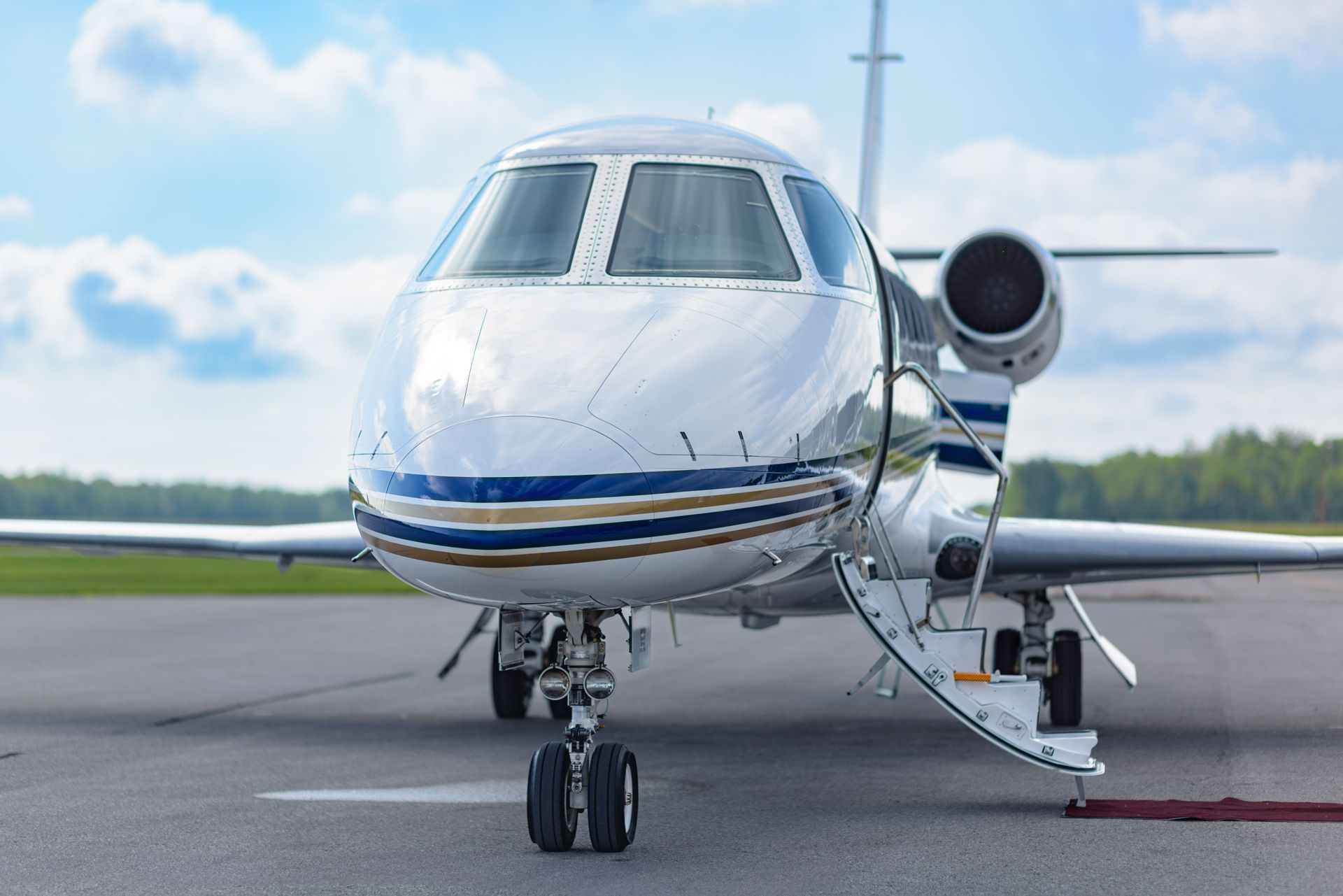 White private jet on runway with boarding stairs extended, front view