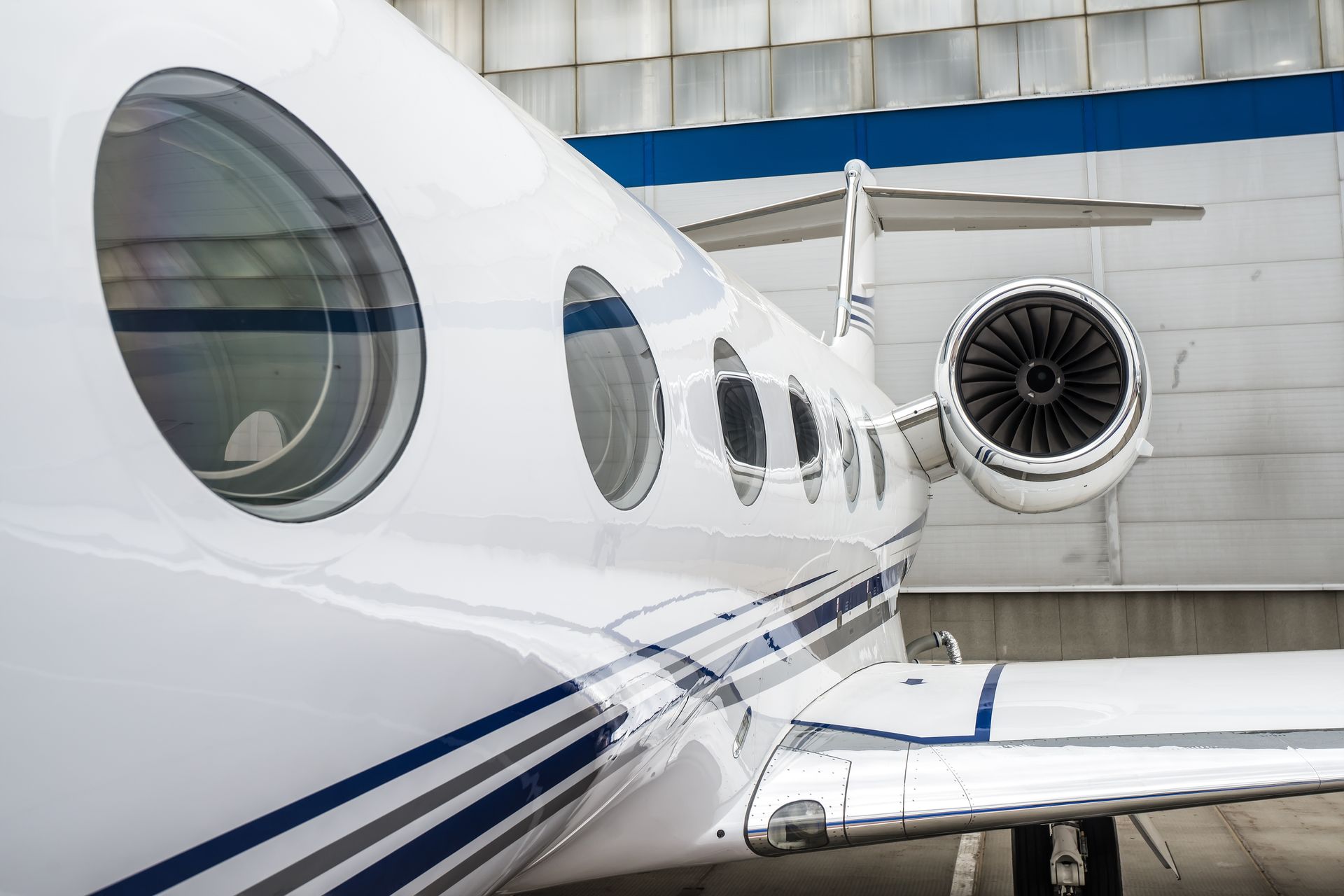 White private jet on tarmac beside another aircraft, showing windows and a jet engine.