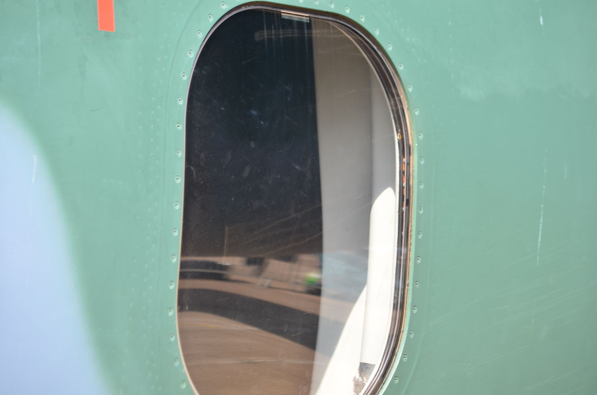 Green train car with an oval window reflecting the platform