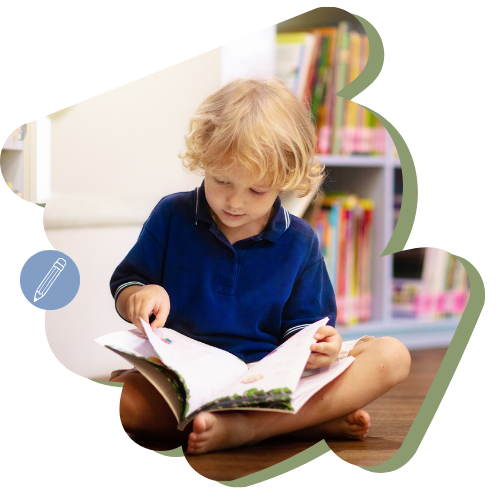 Een kind leest een boek in een klaslokaal, zittend met de benen gekruist, met boekenplanken op de achtergrond.