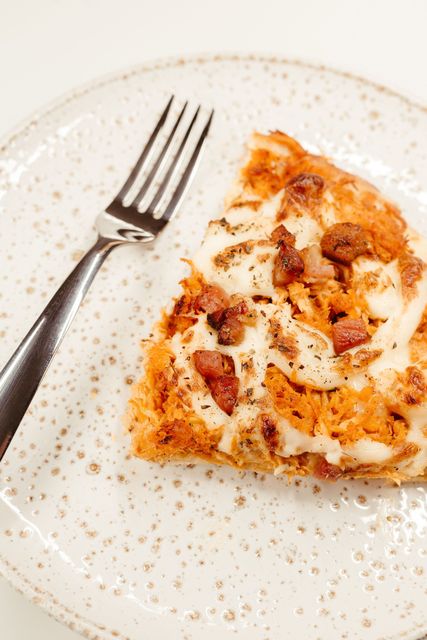 Slice of pizza on a speckled white plate with a fork beside it