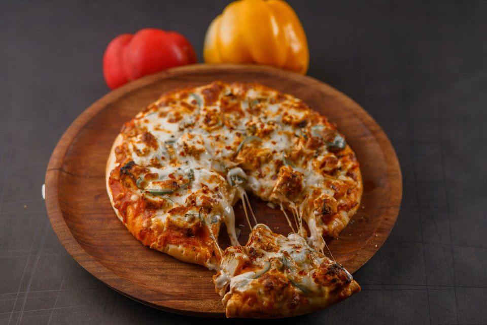 Cheesy pizza on a wooden board with a slice being lifted, against a dark background with red and orange peppers