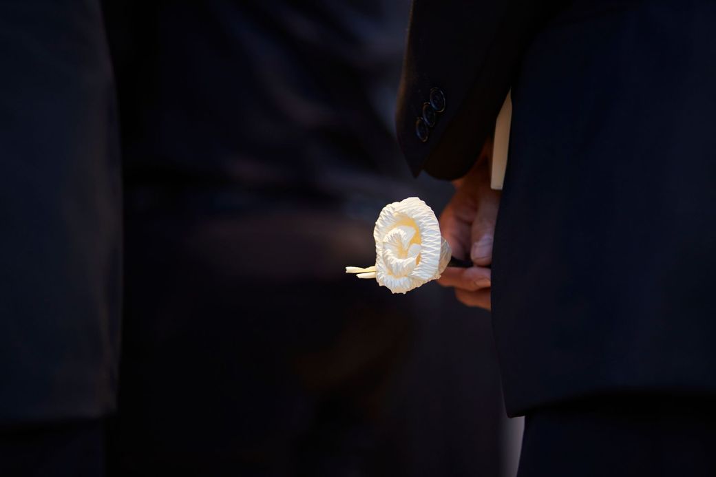 Un uomo in giacca e cravatta tiene in mano una rosa bianca.