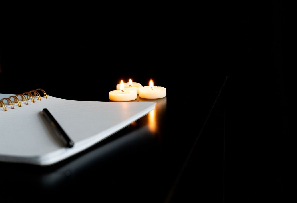 Un quaderno con una penna e tre candele accese su un tavolo.