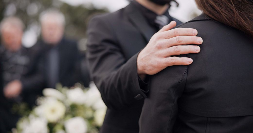 Un uomo tiene la spalla di una donna a un funerale.
