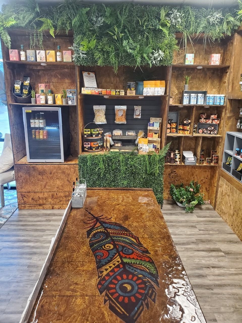 Wood-paneled café shelf display with teas, snacks, and hanging greenery, beside a patterned rug on the floor