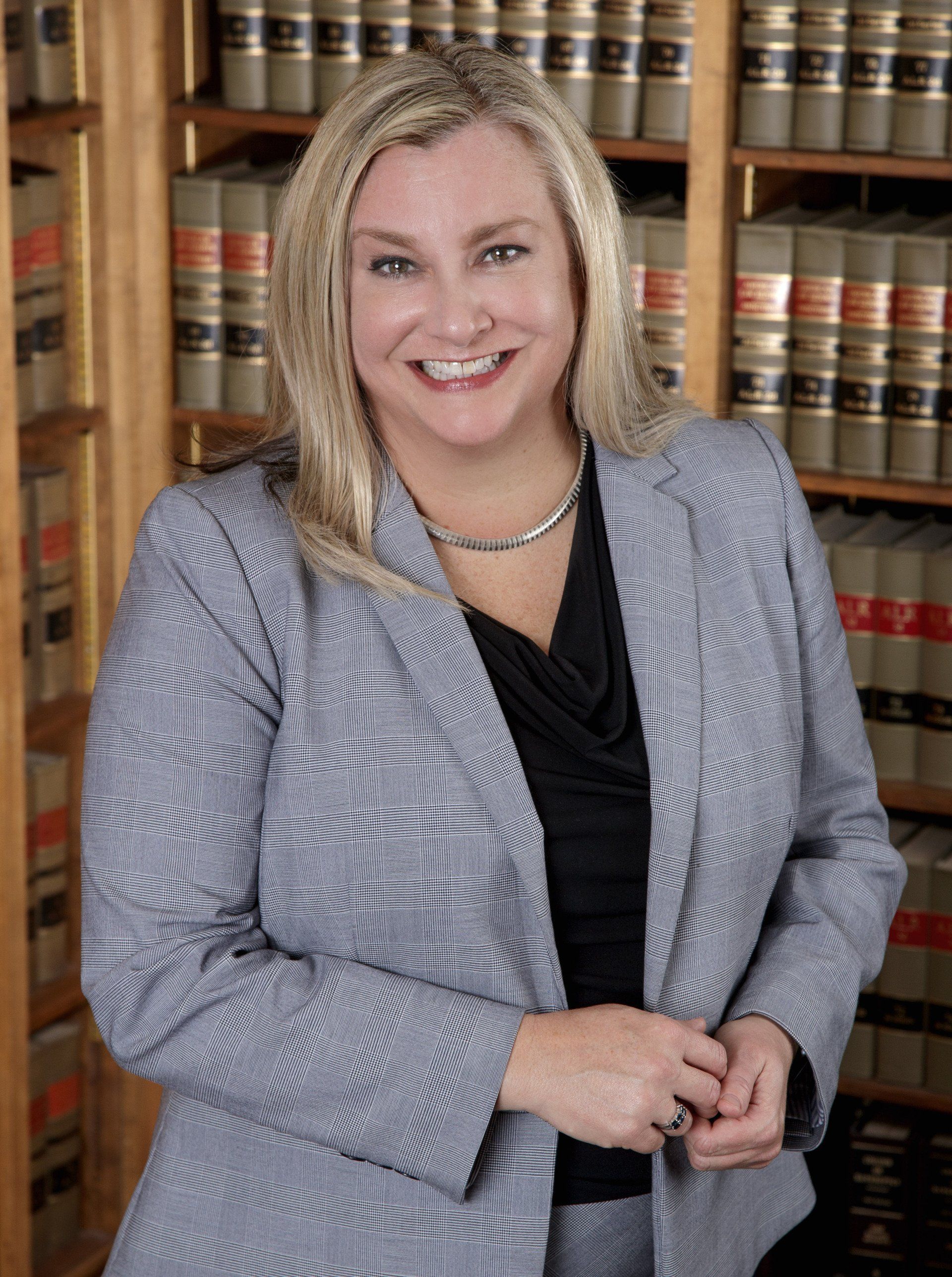 A woman in a suit is standing in front of a bookshelf.