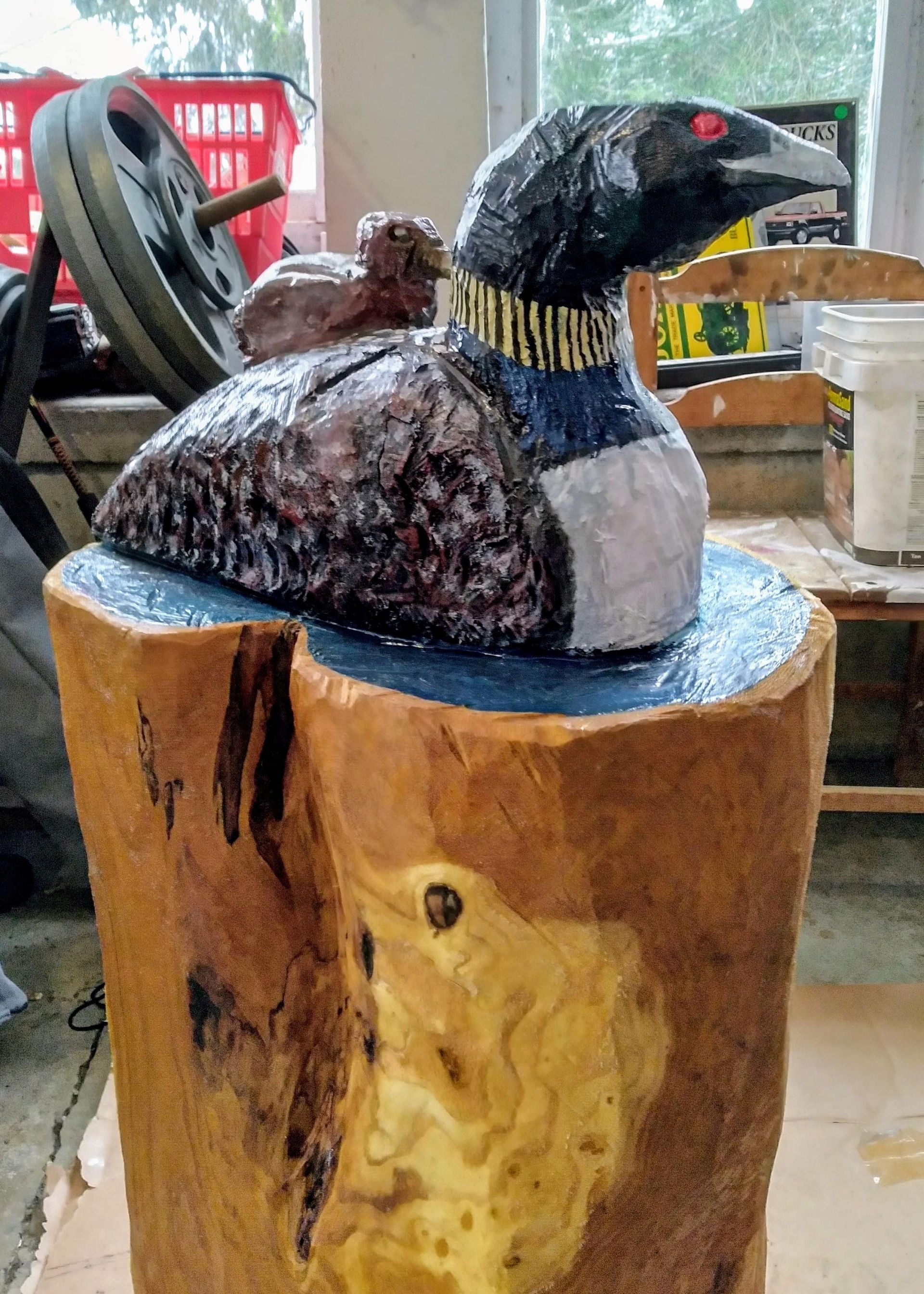 Hand-carved loon sculpture with black-and-white plumage on a wood stump stand indoors