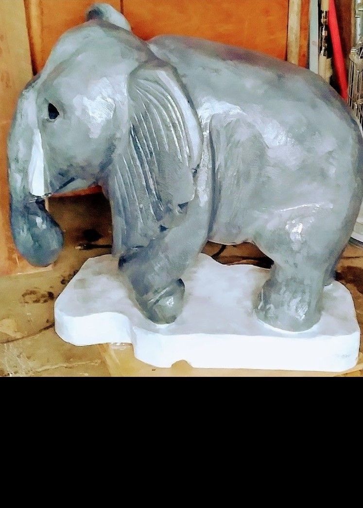 Silver elephant statue on a white base, shown in profile against a wooden background