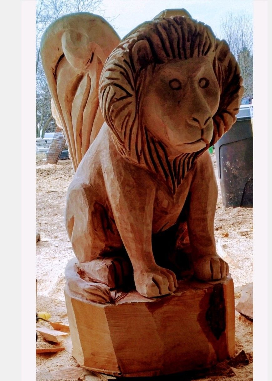 Wooden lion statue on a carved base, shown outdoors in daylight