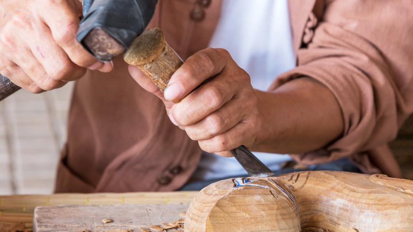 Hands carving wood with a chisel and hammer on a workbench