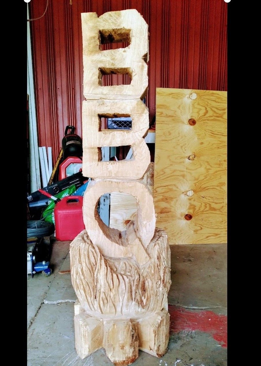 Wooden carved sculpture with stacked circular and rectangular shapes, standing indoors against a wood backdrop