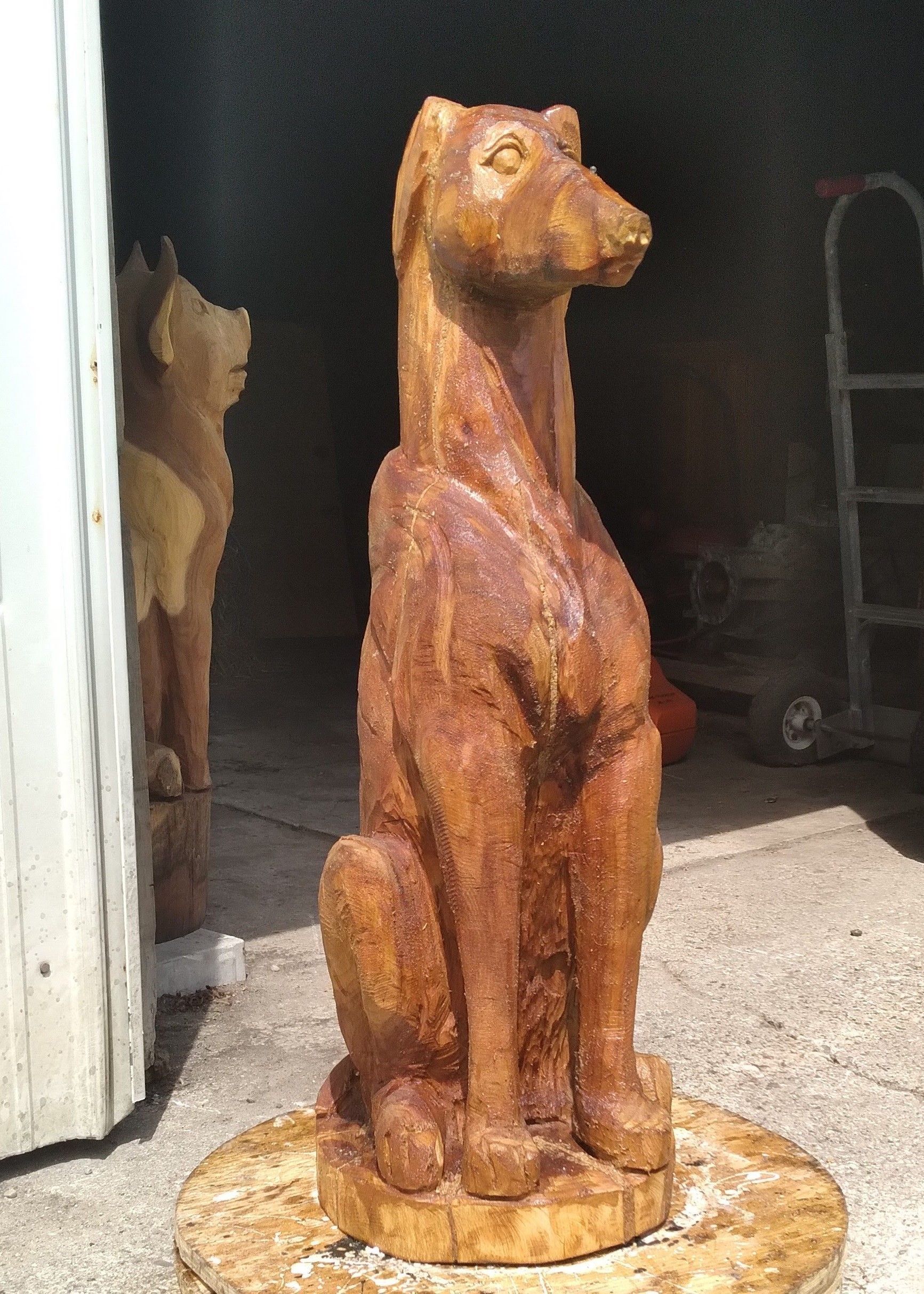 Rust-colored carved wooden dog sculpture standing on a round base in a doorway, with another sculpture behind it