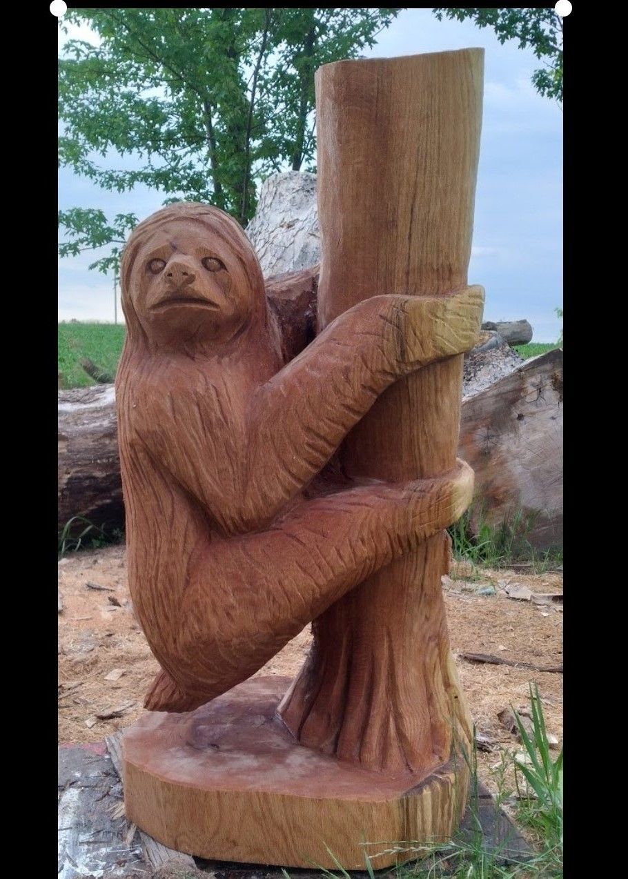 Wooden orangutan sculpture hugging a tree trunk outdoors, with rocks and trees in the background