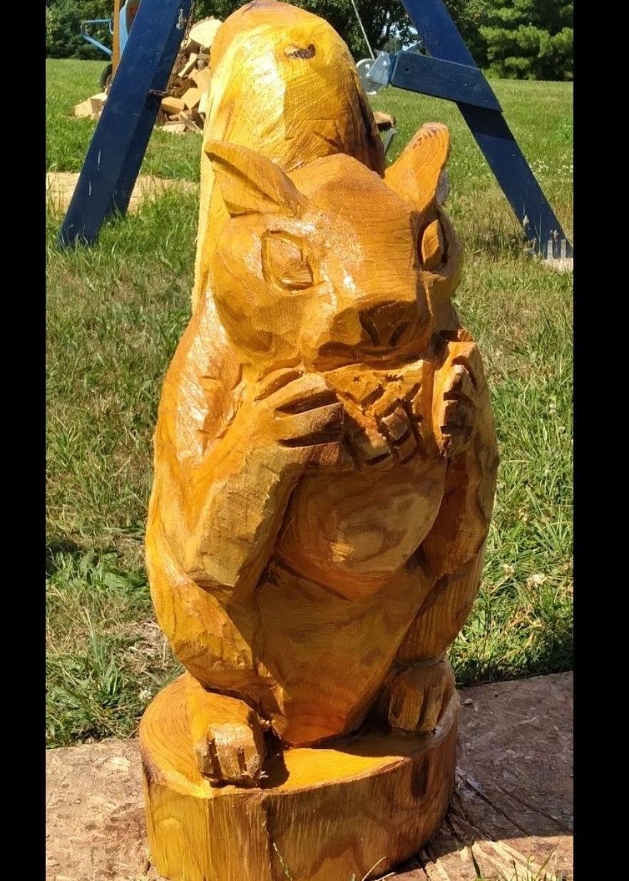 Golden carved wooden squirrel statue standing outdoors on a pedestal in sunlight