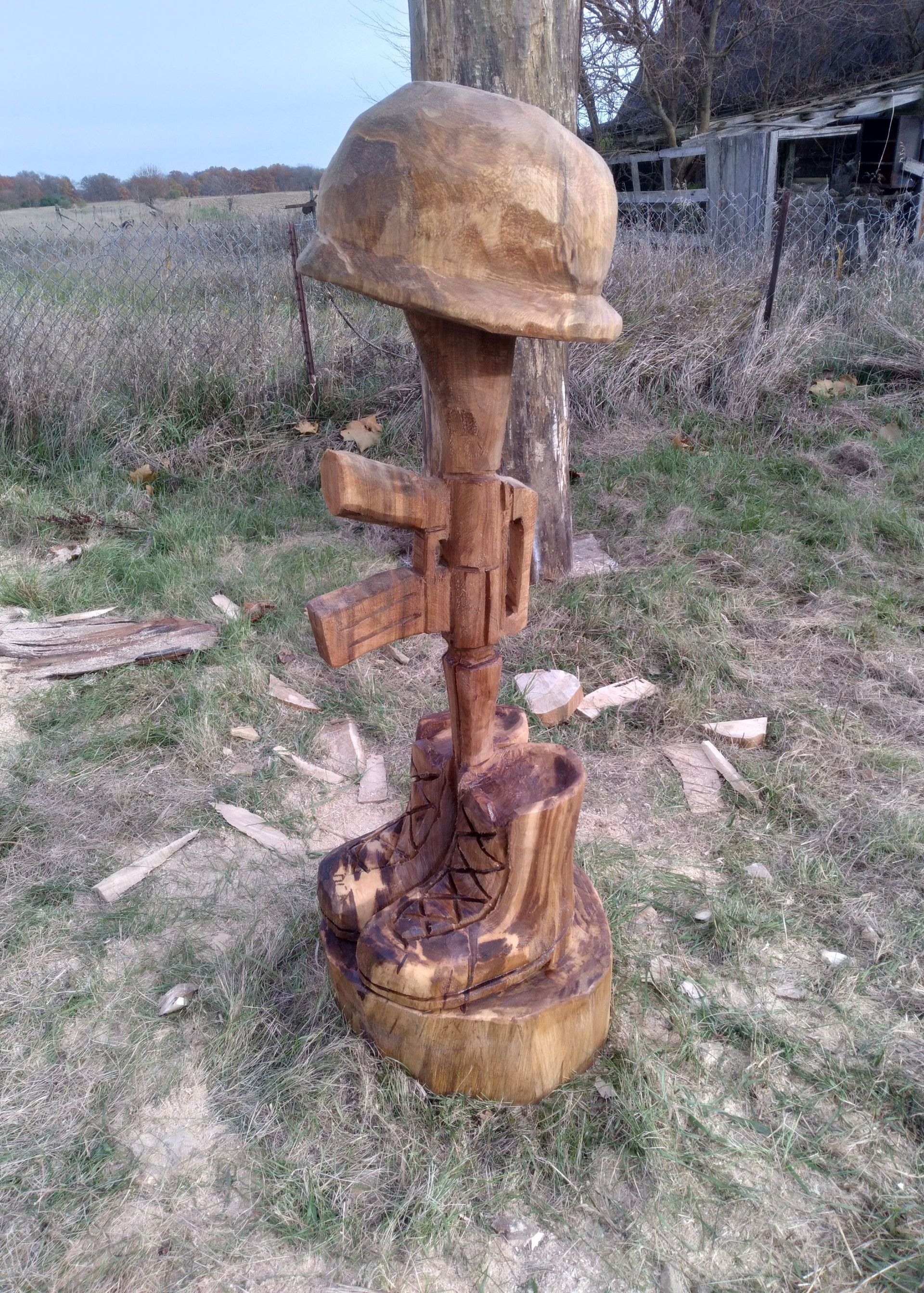 Hand-carved wooden sculpture with a rounded cap, standing outdoors on grass near a fence.