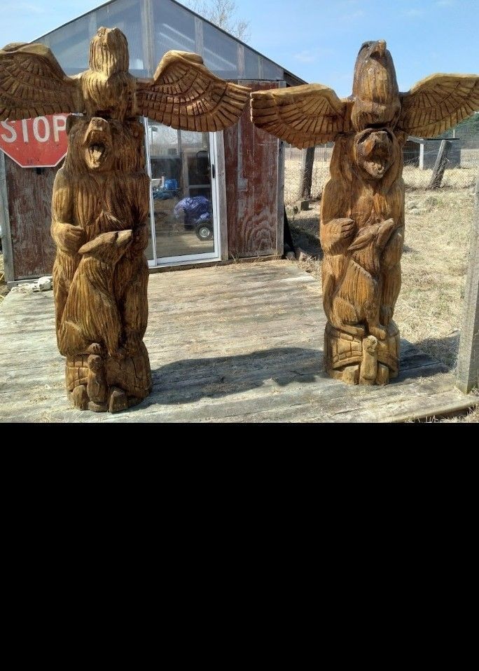 Two carved wooden totem poles flanking a glass entrance with a stop sign in the background