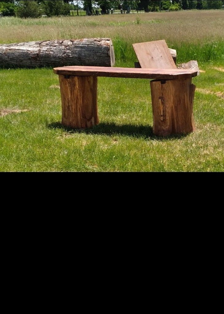 Rustic log bench on grass in a sunny field with a large fallen log behind it.