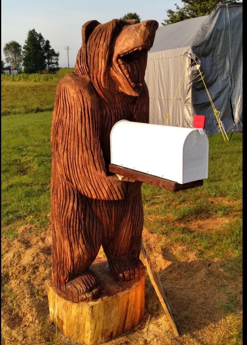 Wooden bear statue holding a white mailbox outdoors near a tent.