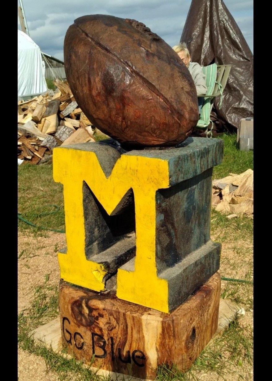 A large yellow “M” sculpture atop stacked stone blocks in an outdoor setting.