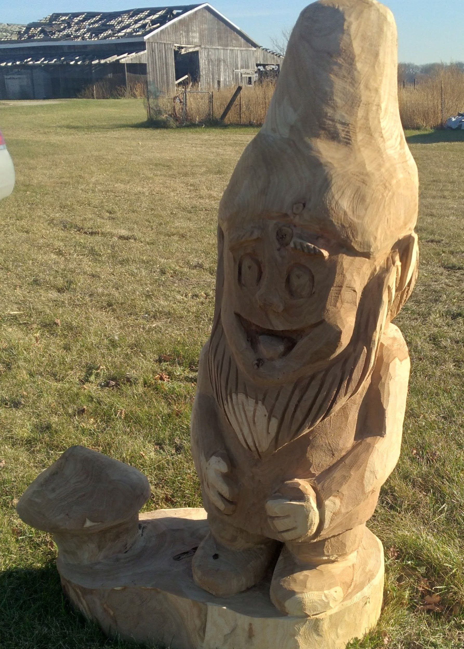 Carved wooden gnome statue in a grassy yard, with a small house in the background.
