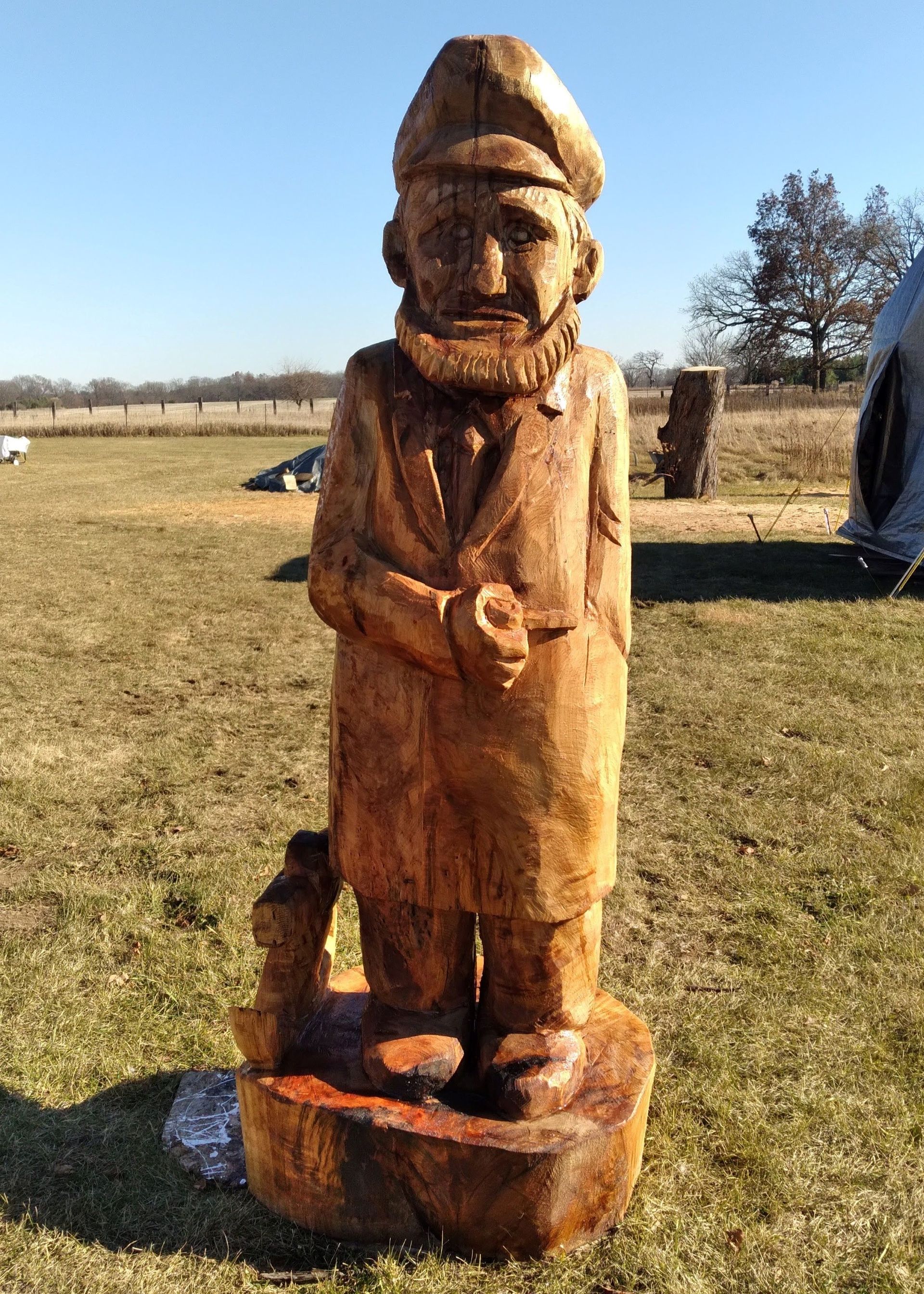 Wooden carved statue of a man standing outdoors in a grassy field