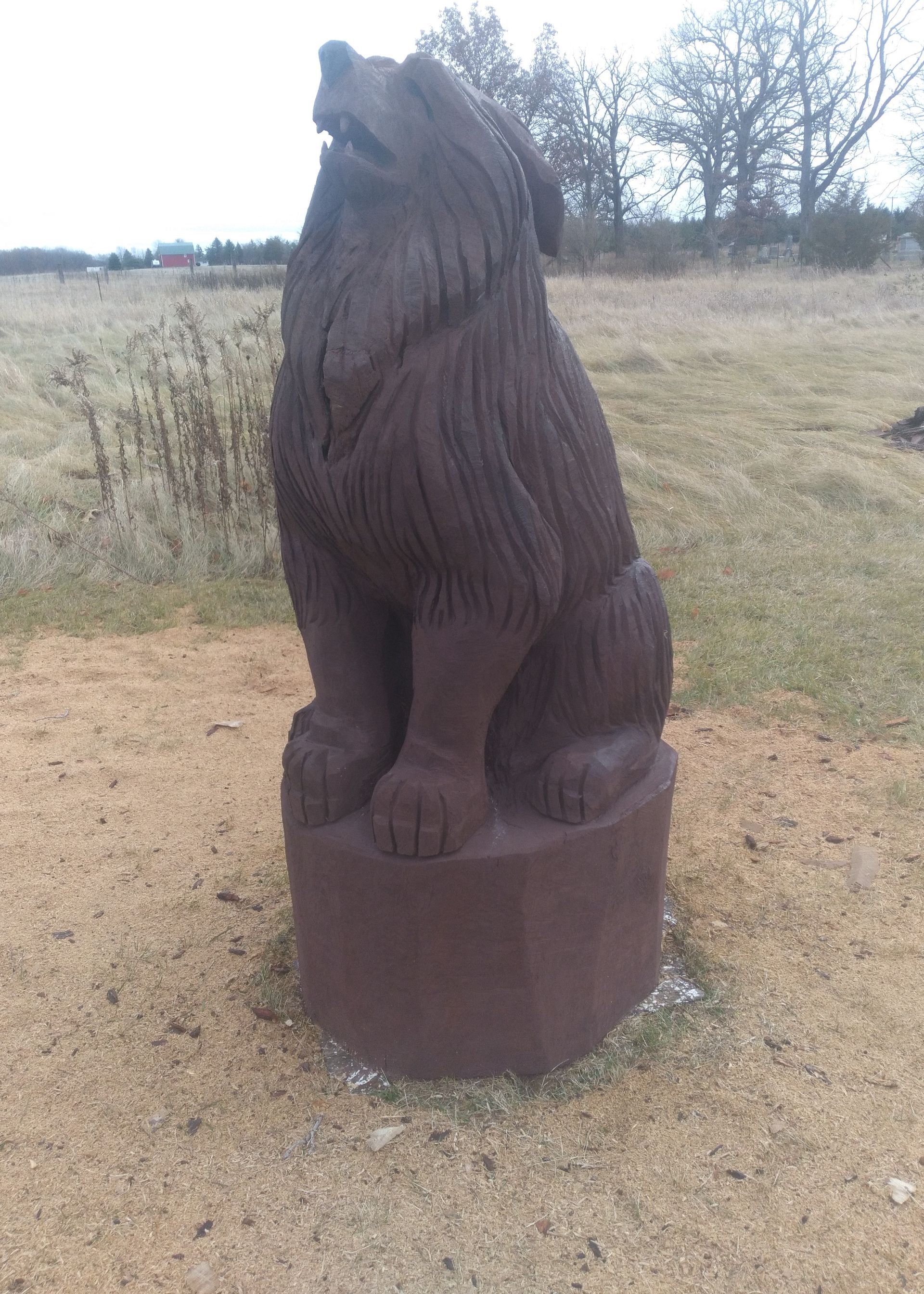 Dark wooden bear statue sitting on a round base in a grassy field
