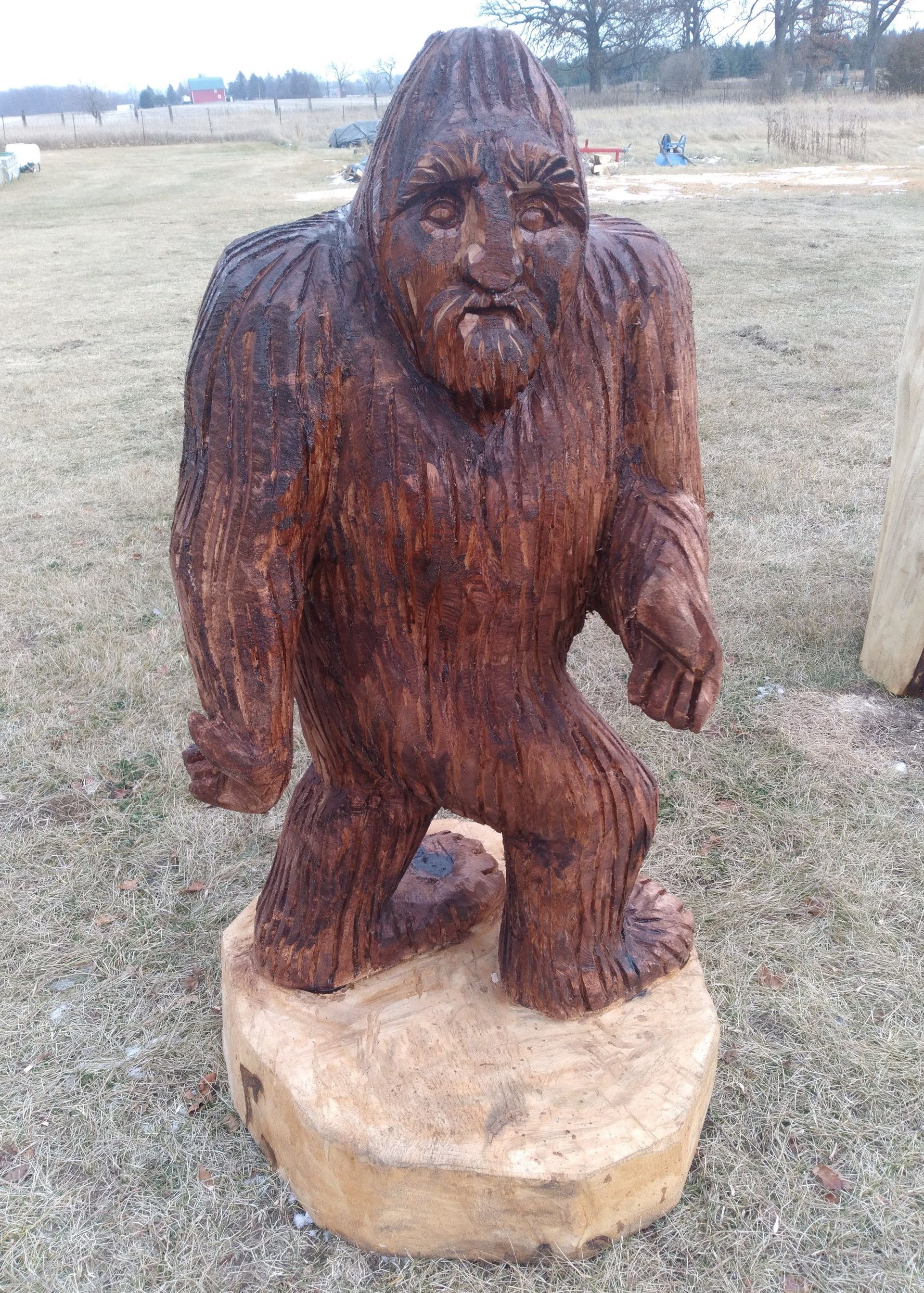Wooden Bigfoot statue standing on a round base in a grassy field