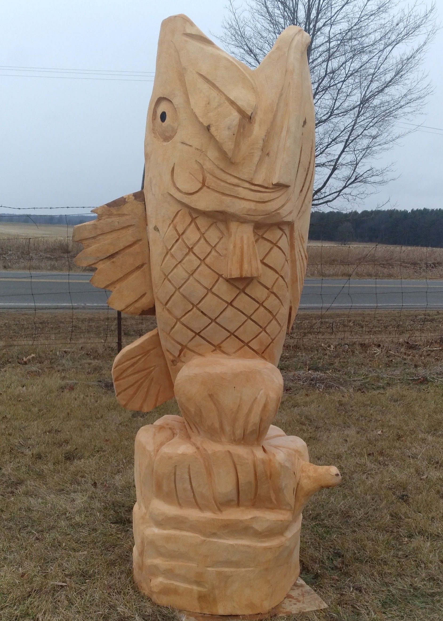Wooden fish carving on a base in an outdoor field under a cloudy sky